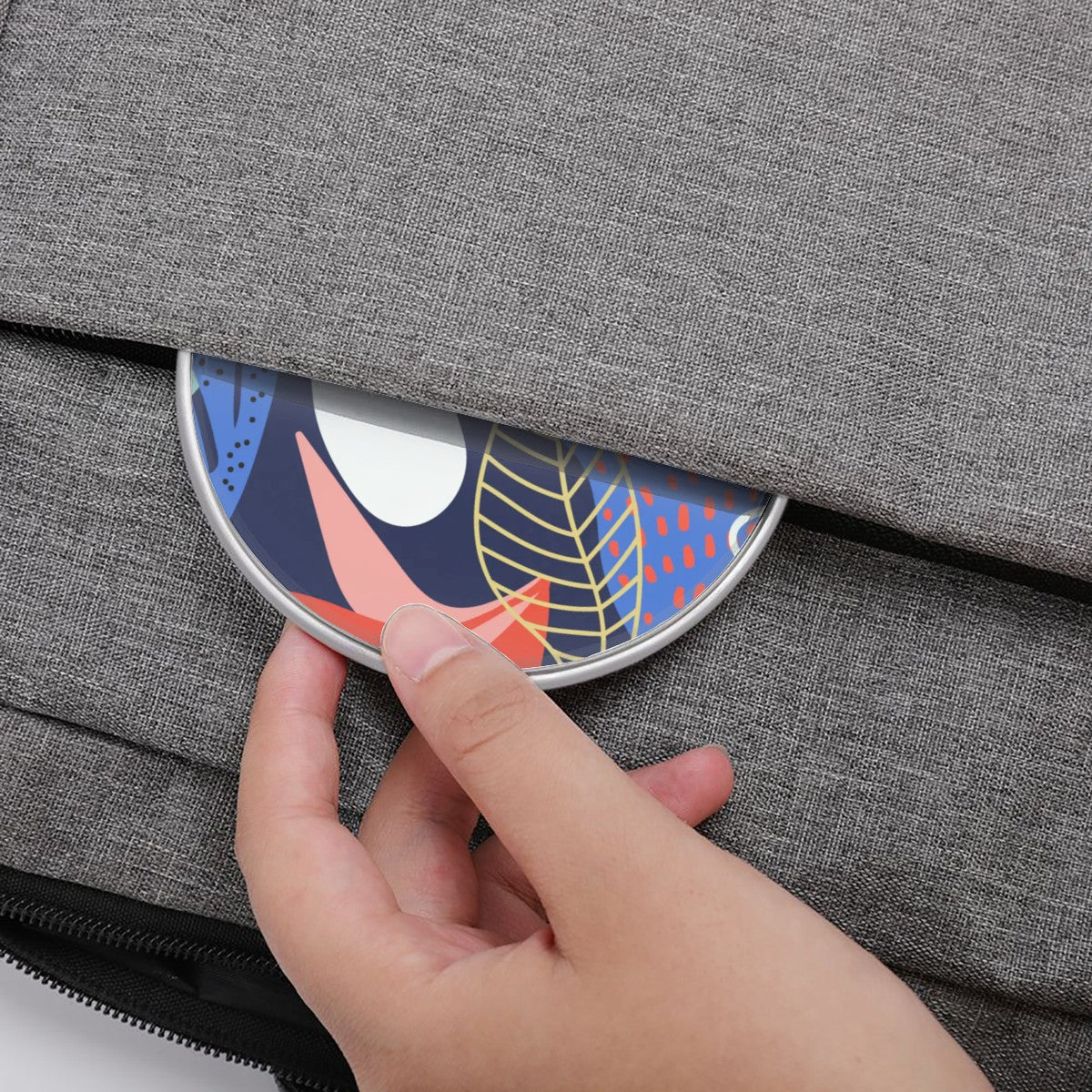 Hand placing a colorful circular object with leaf patterns into a gray textured bag.