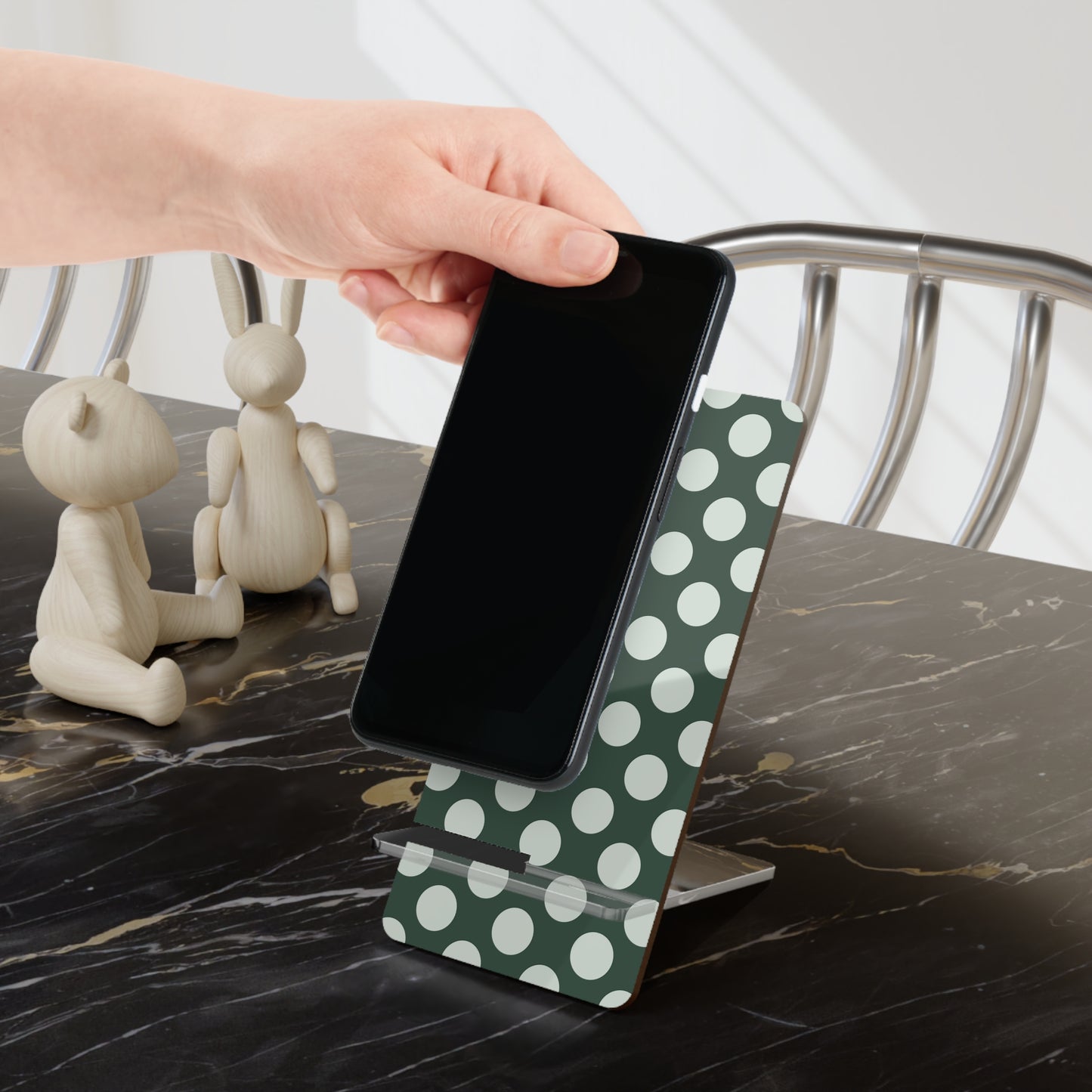 Hand holding a smartphone on a green polka dot stand with decorative items in the background