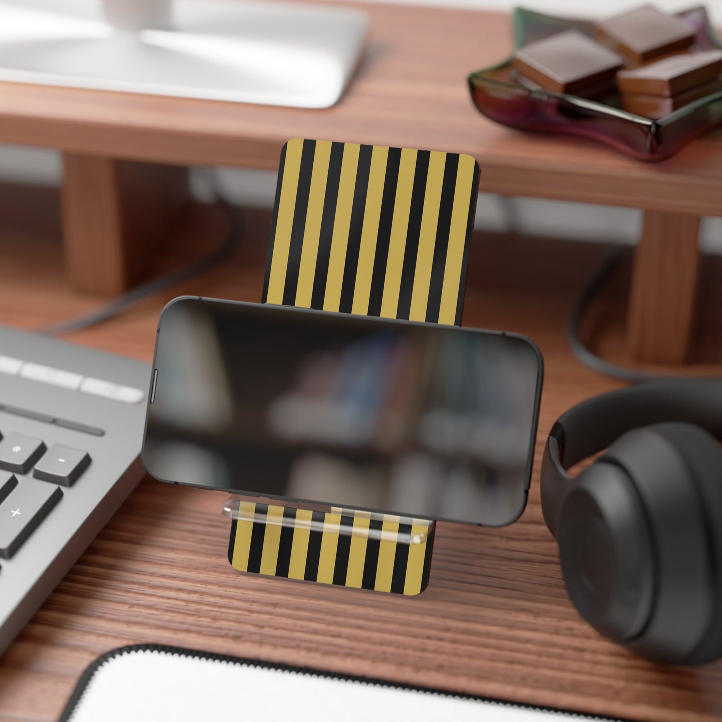 Phone stand with striped design on a desk with keyboard, mouse, and headphones.
