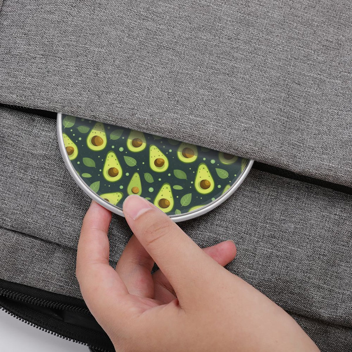 Hand placing a round coaster with avocado pattern on a gray textured surface