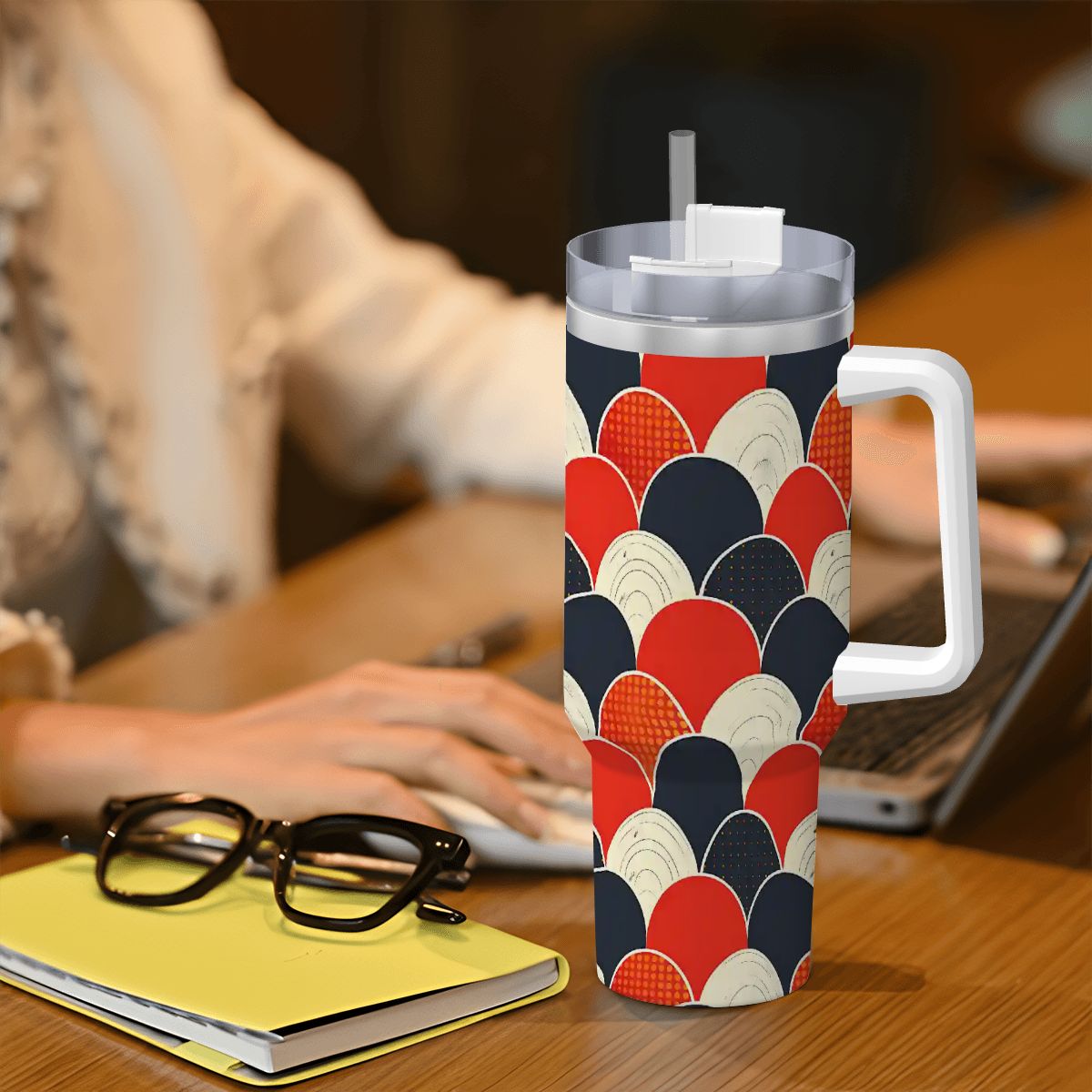 Colorful insulated mug with geometric pattern on a desk with glasses and notebook.