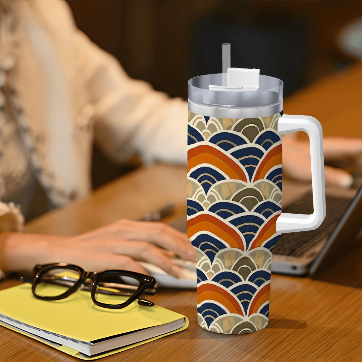 Colorful patterned mug with handle on a desk next to glasses and a notebook