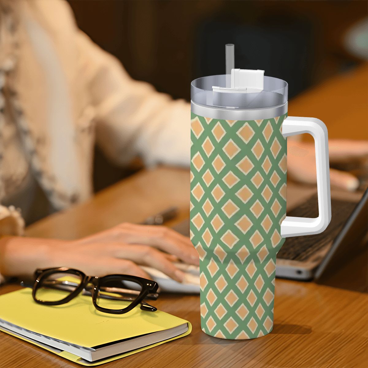 Person using a laptop with a patterned tumbler on a desk