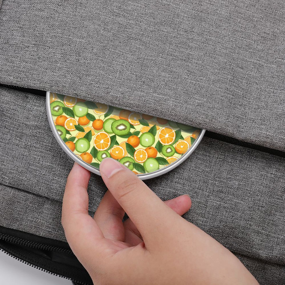 Hand placing a round fruit-patterned item into a gray bag
