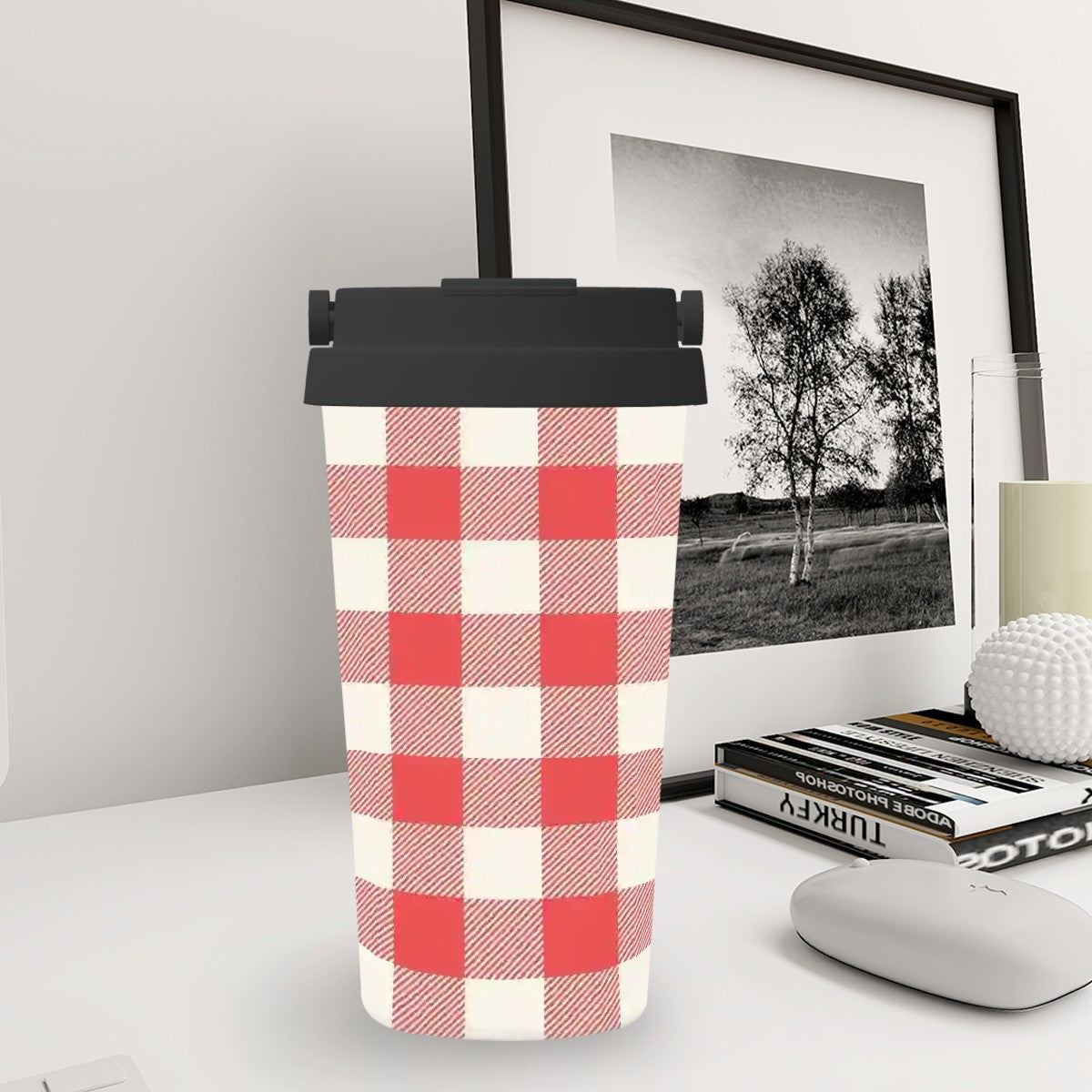 Red and white checkered tumbler on a desk with a framed picture in the background