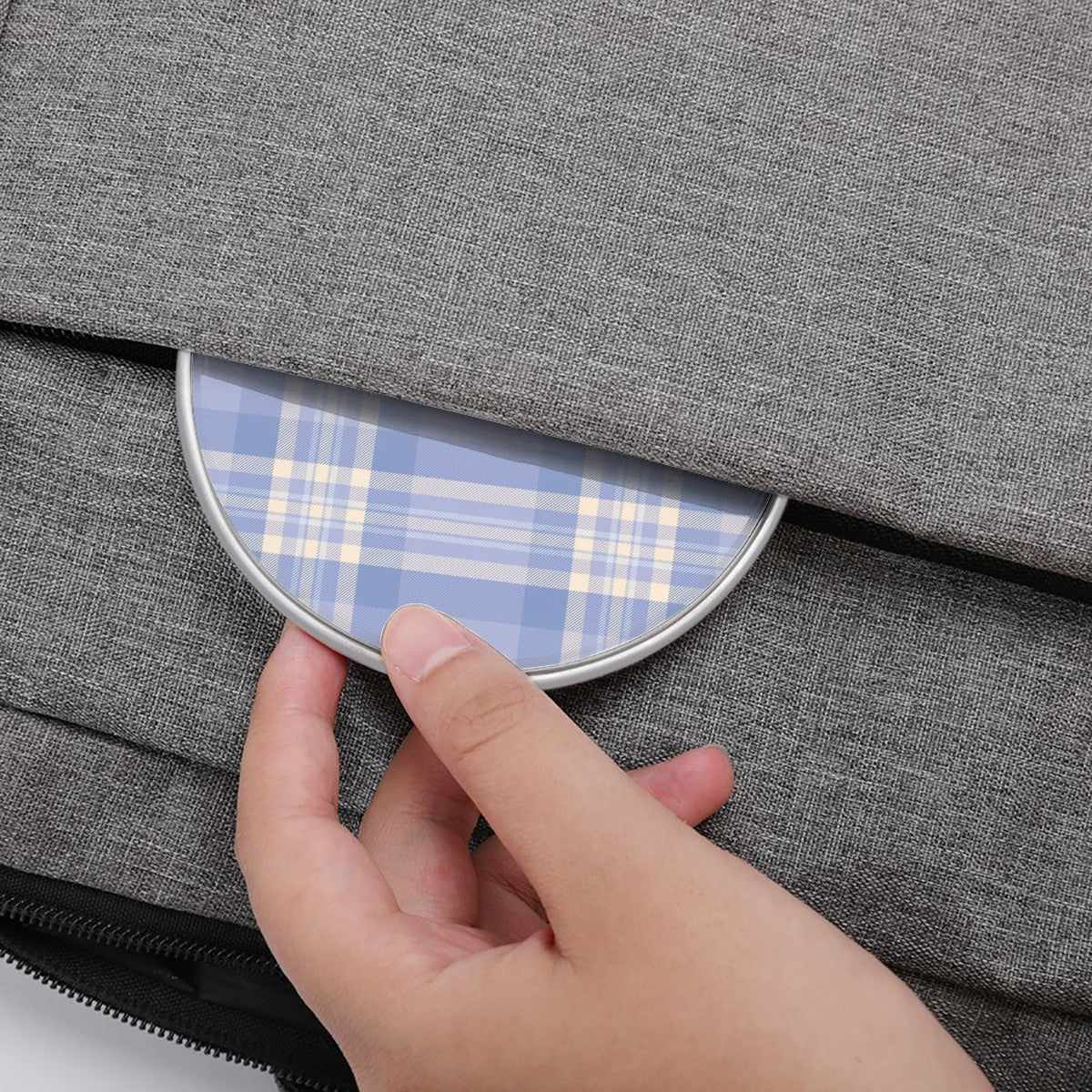 Hand placing a small round mirror with plaid pattern into a gray fabric bag.