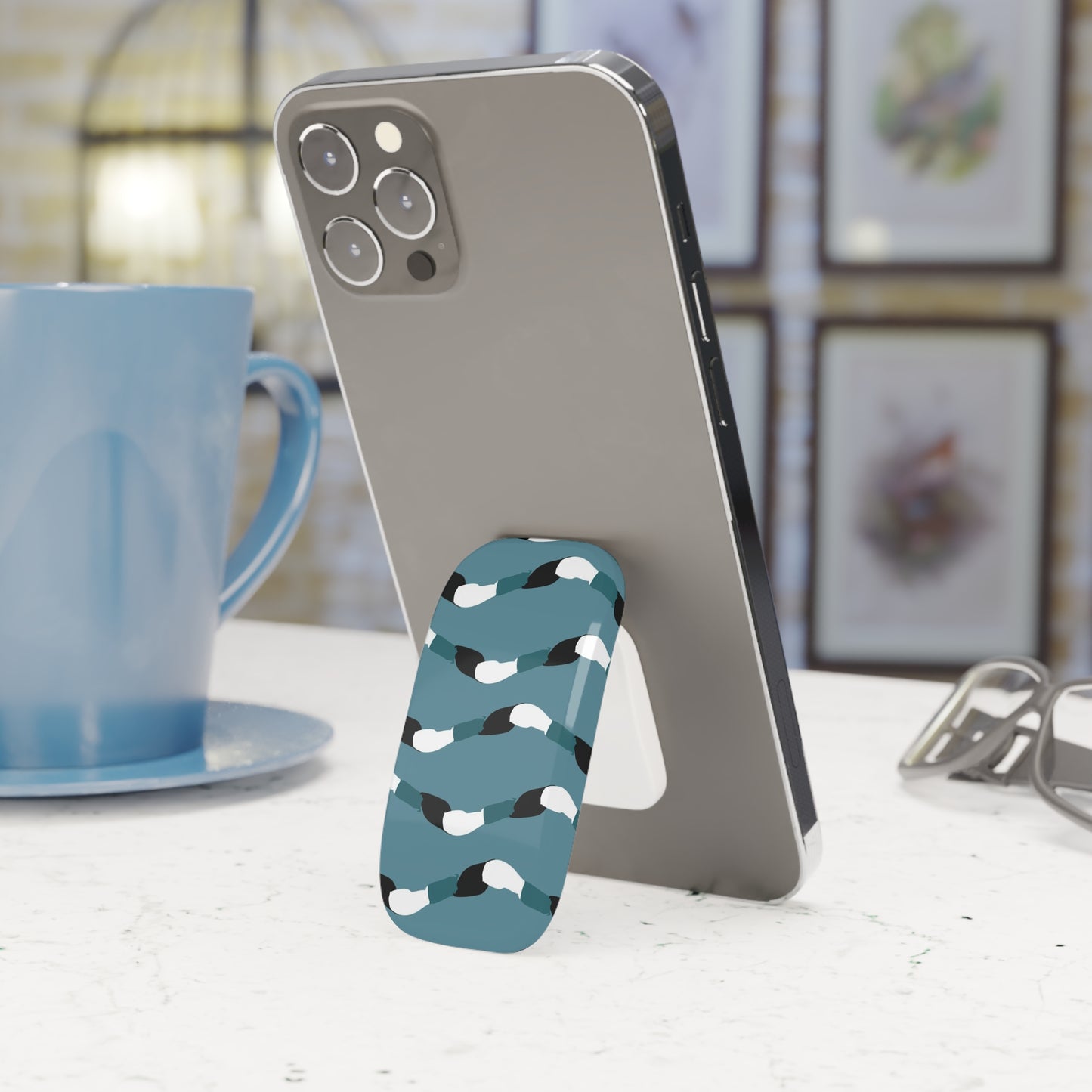 Phone with a blue and white patterned stand on a table next to a blue mug.