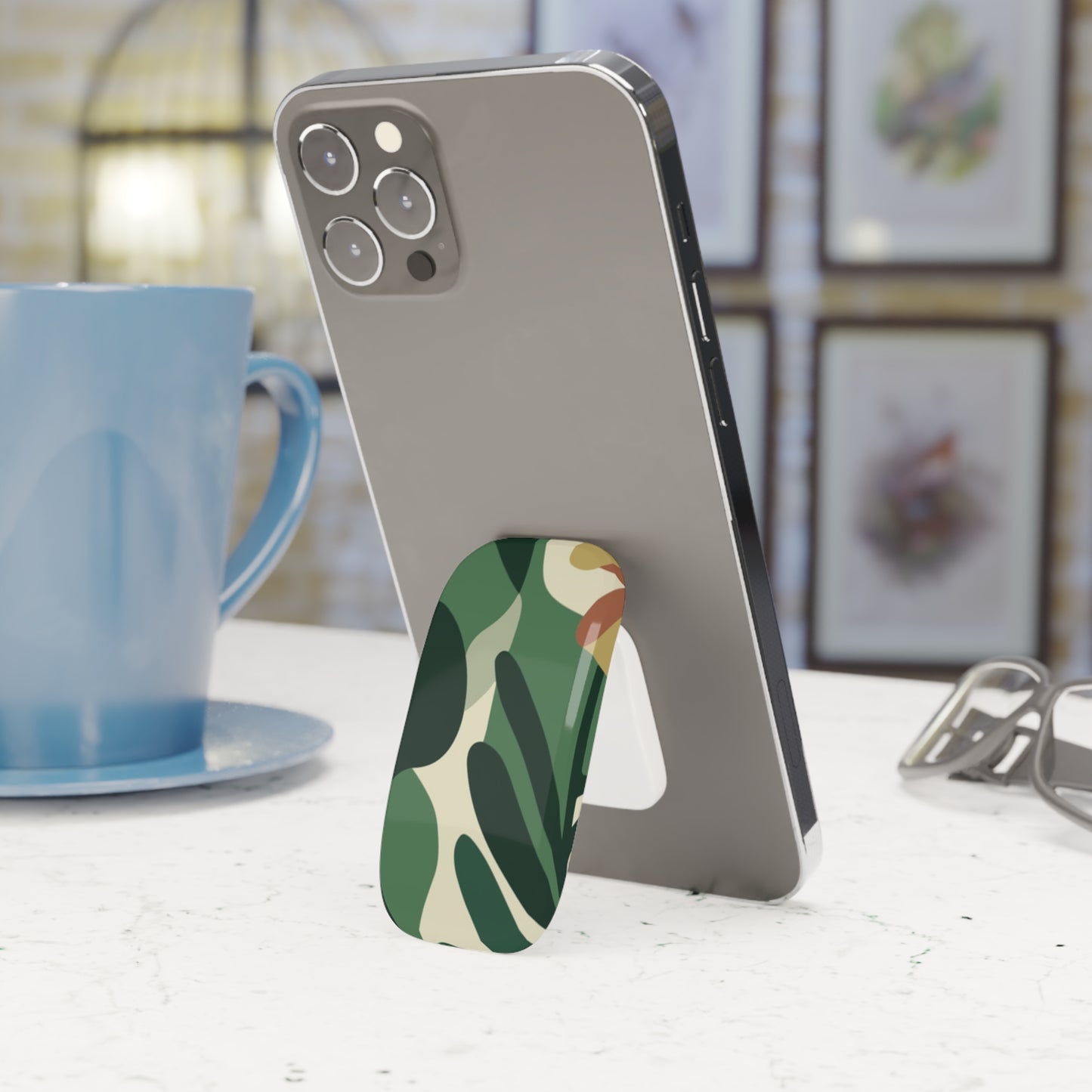 Phone with a camouflage stand on a table next to a blue mug