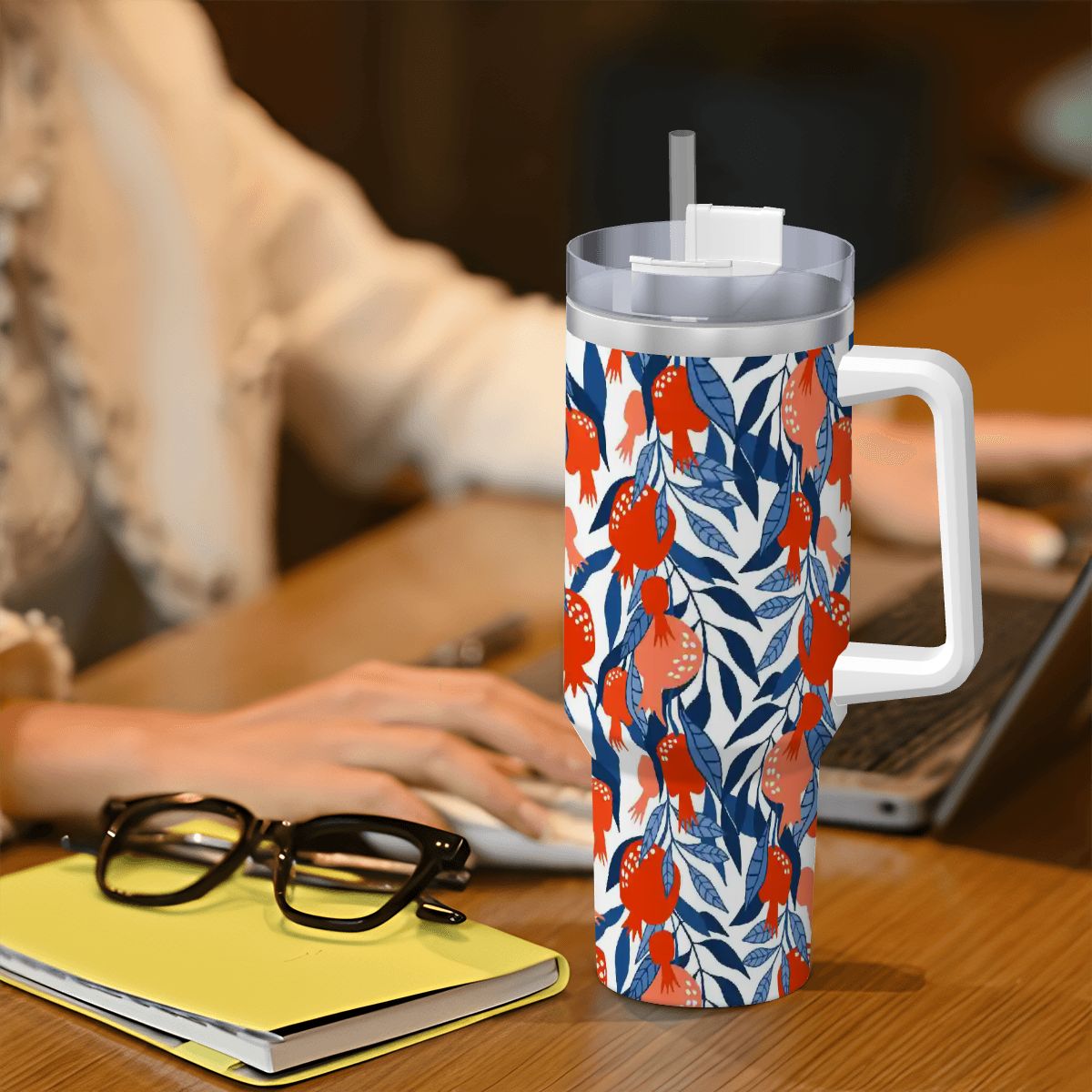 Tumbler with floral pattern on a desk with a person using a laptop.