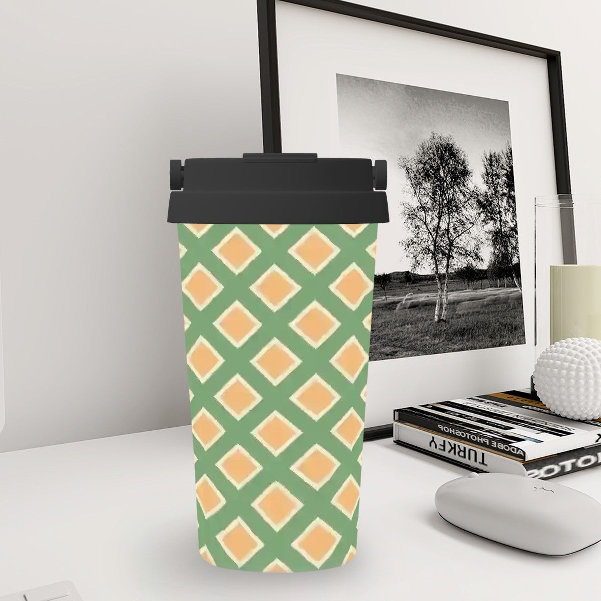 Green and orange patterned tumbler on a desk with a framed picture in the background