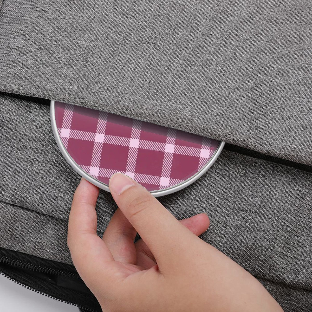 Hand opening a gray fabric bag with a pink plaid lining