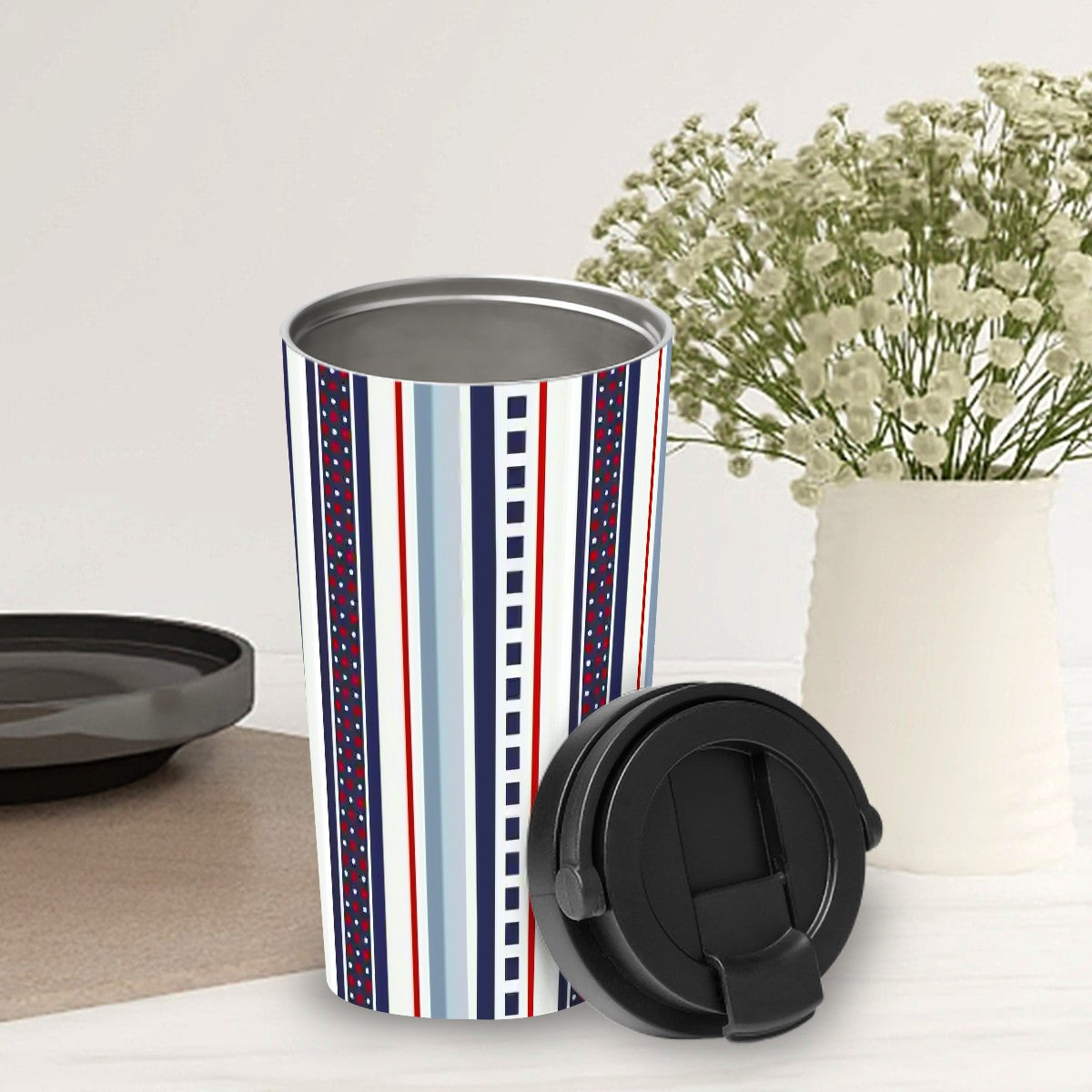 Travel mug with striped design on a white surface with a vase of flowers in the background