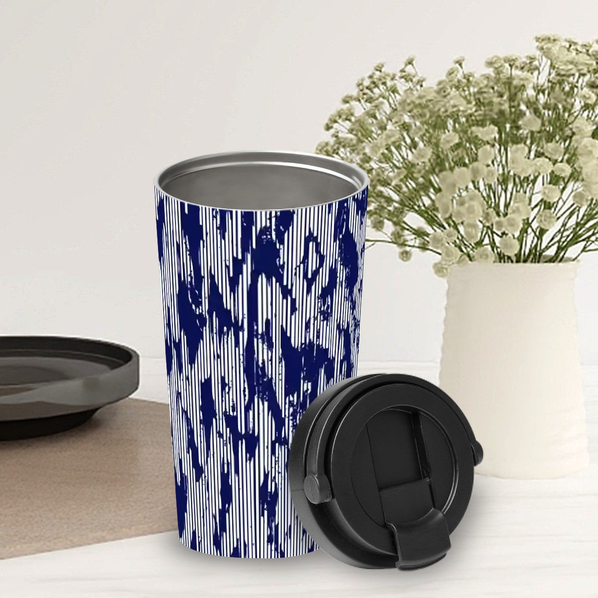 Blue and white patterned tumbler with black lid on a light surface with flowers in the background