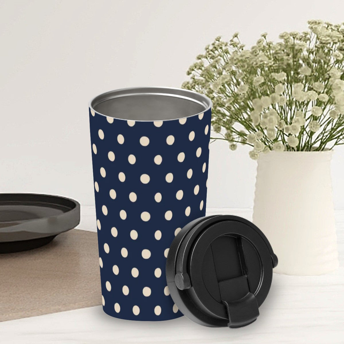 Navy blue tumbler with white polka dots on a light surface with a vase of flowers in the background.