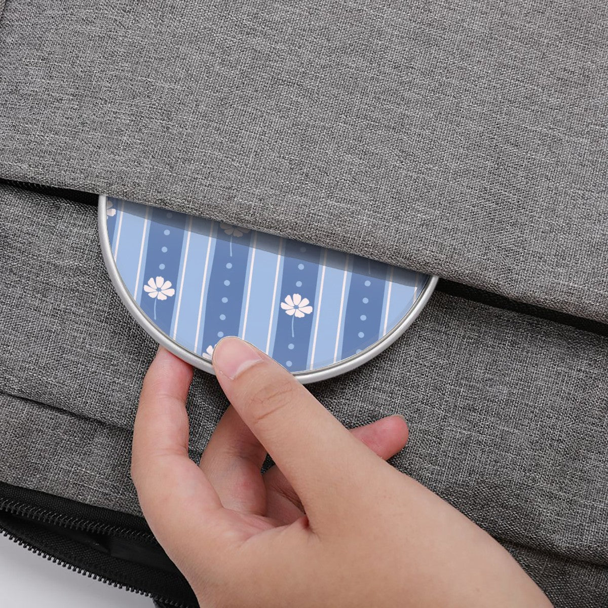 Hand opening a gray textured bag with a blue and white patterned flap.