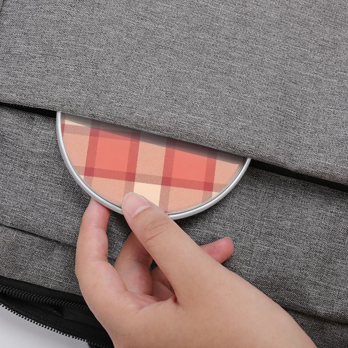 Hand holding a round compact mirror with plaid design against a gray textured background