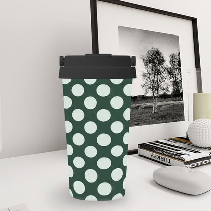 Green tumbler with white polka dots on a desk with books and a framed picture in the background.