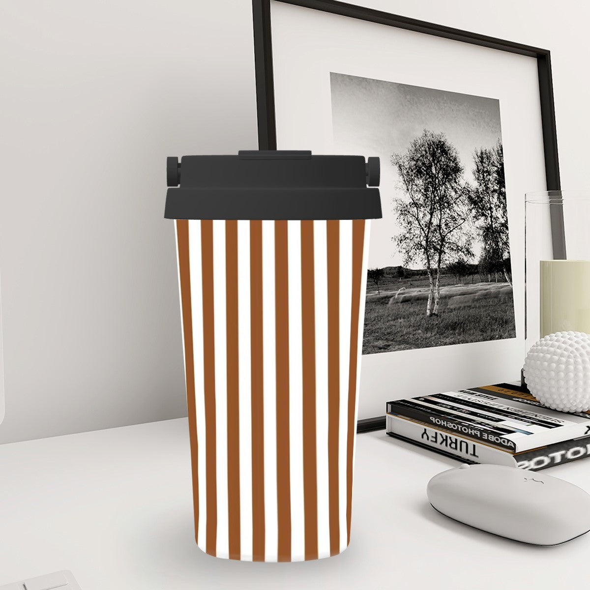 Striped travel mug on a desk with a framed picture and books in the background