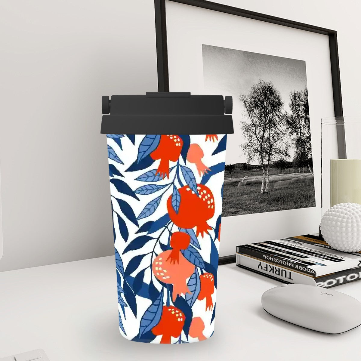 Tumbler with floral design on a desk next to a framed picture and books.