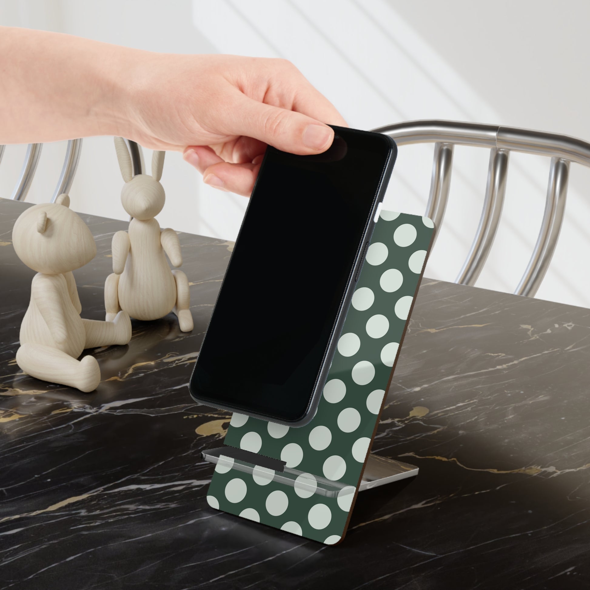 Hand holding a smartphone on a green polka dot stand with decorative items in the background