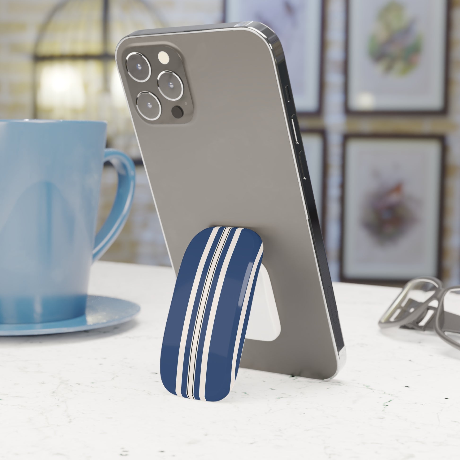 Phone with a blue and white striped stand on a table next to a blue mug.
