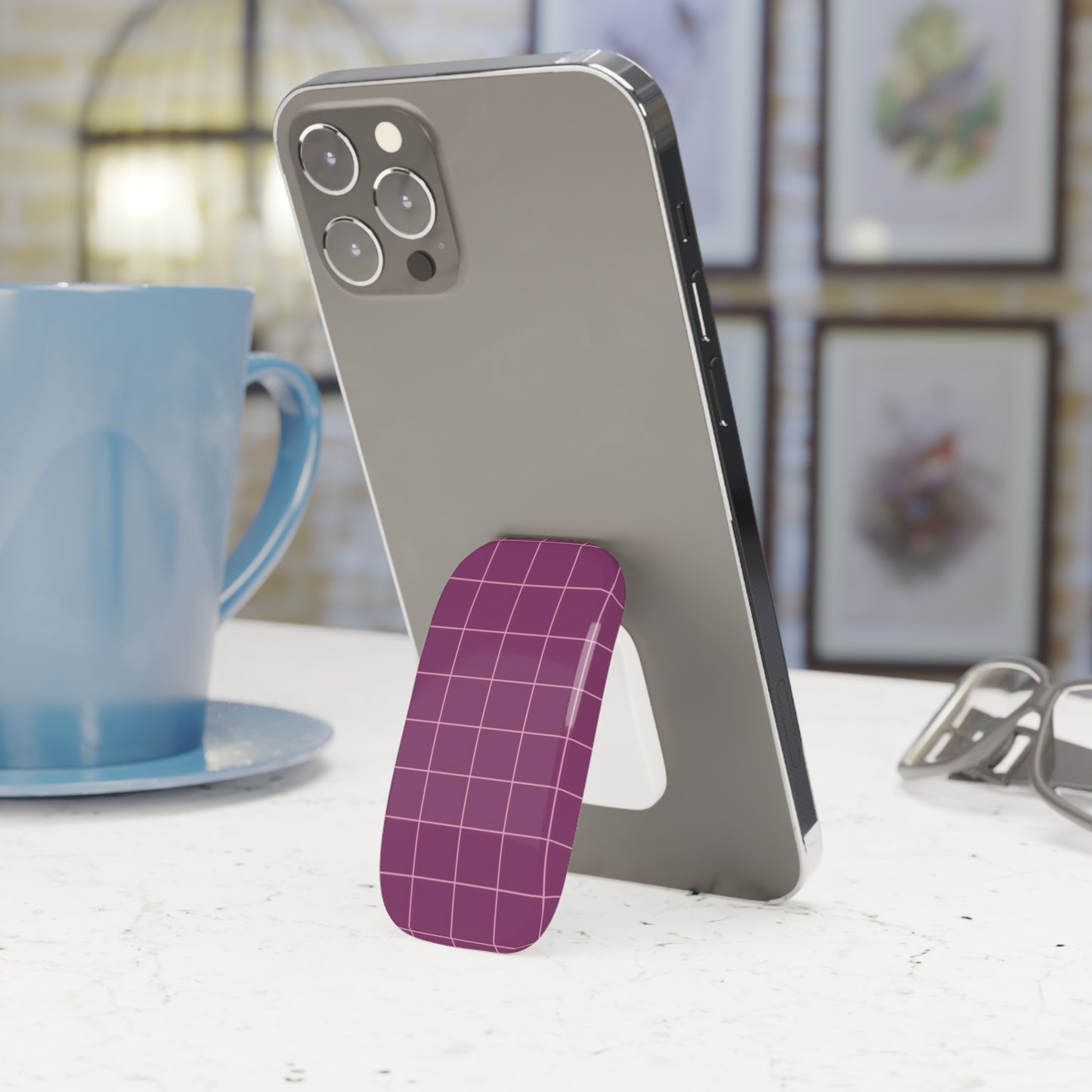 Phone with a purple stand on a surface next to a blue mug