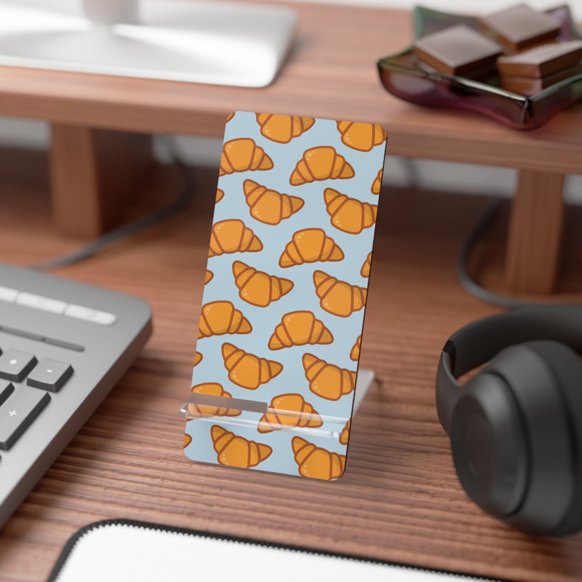 Phone stand with croissant pattern on a desk with keyboard and headphones | Casenari