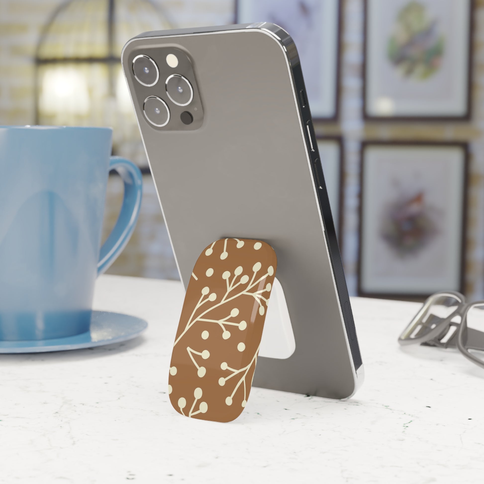 Phone with a decorative stand on a table next to a blue mug