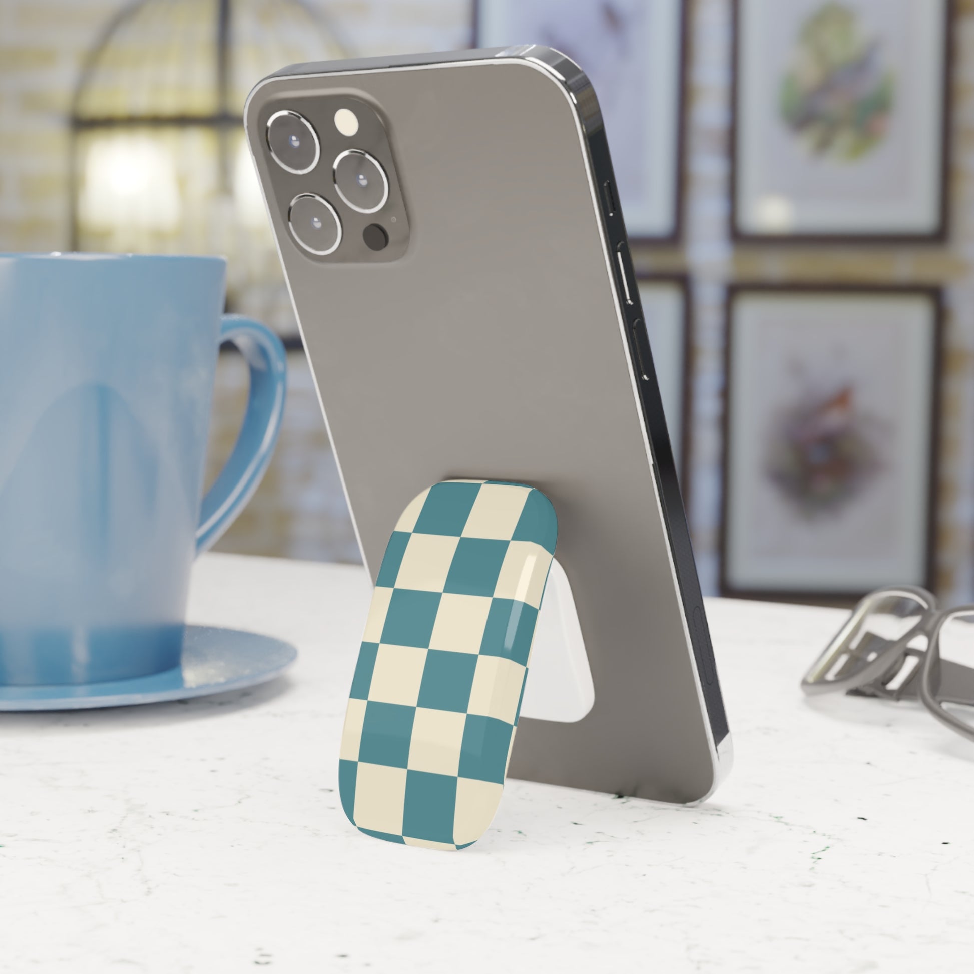 Phone with a checkered phone stand on a table next to a blue mug.