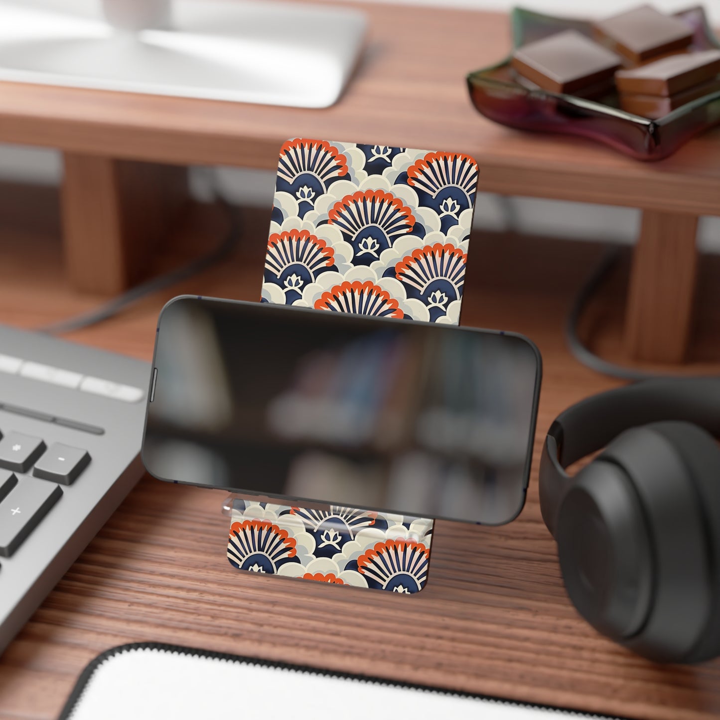Phone stand with decorative pattern on a desk with keyboard, headphones, and books.