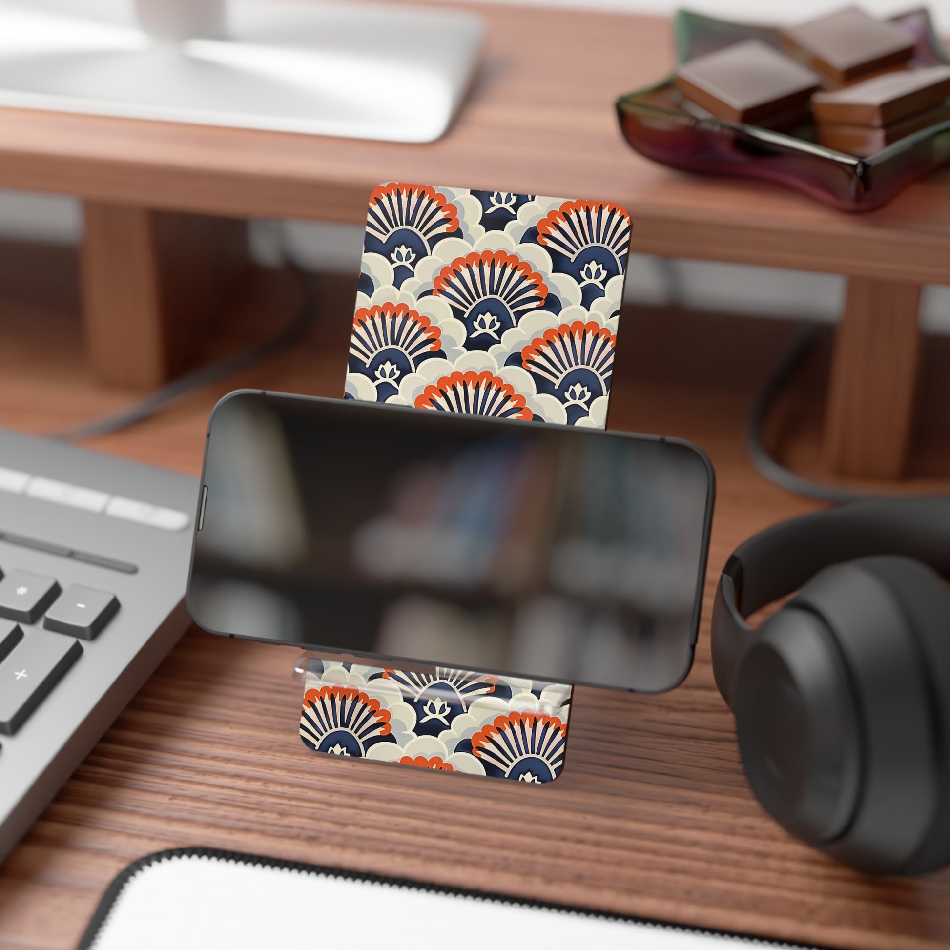 Phone stand with decorative pattern on a desk with keyboard, headphones, and books.