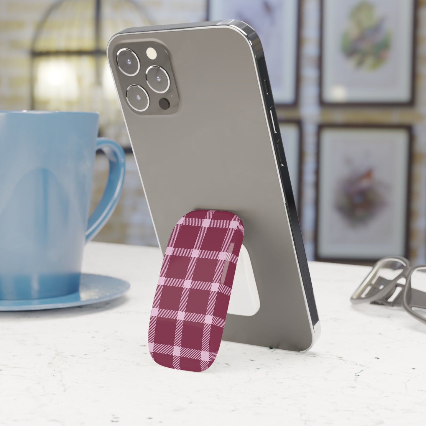 Phone stand with plaid design holding a smartphone next to a blue mug on a table.