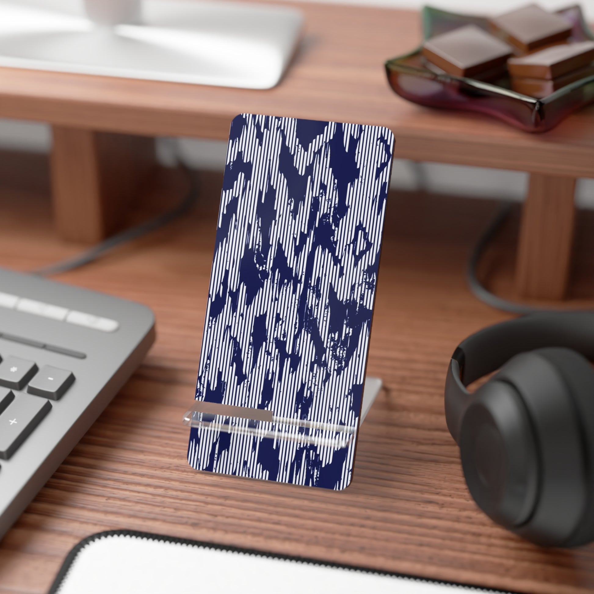 Phone stand with blue abstract pattern on a desk with keyboard, mouse, and headphones.