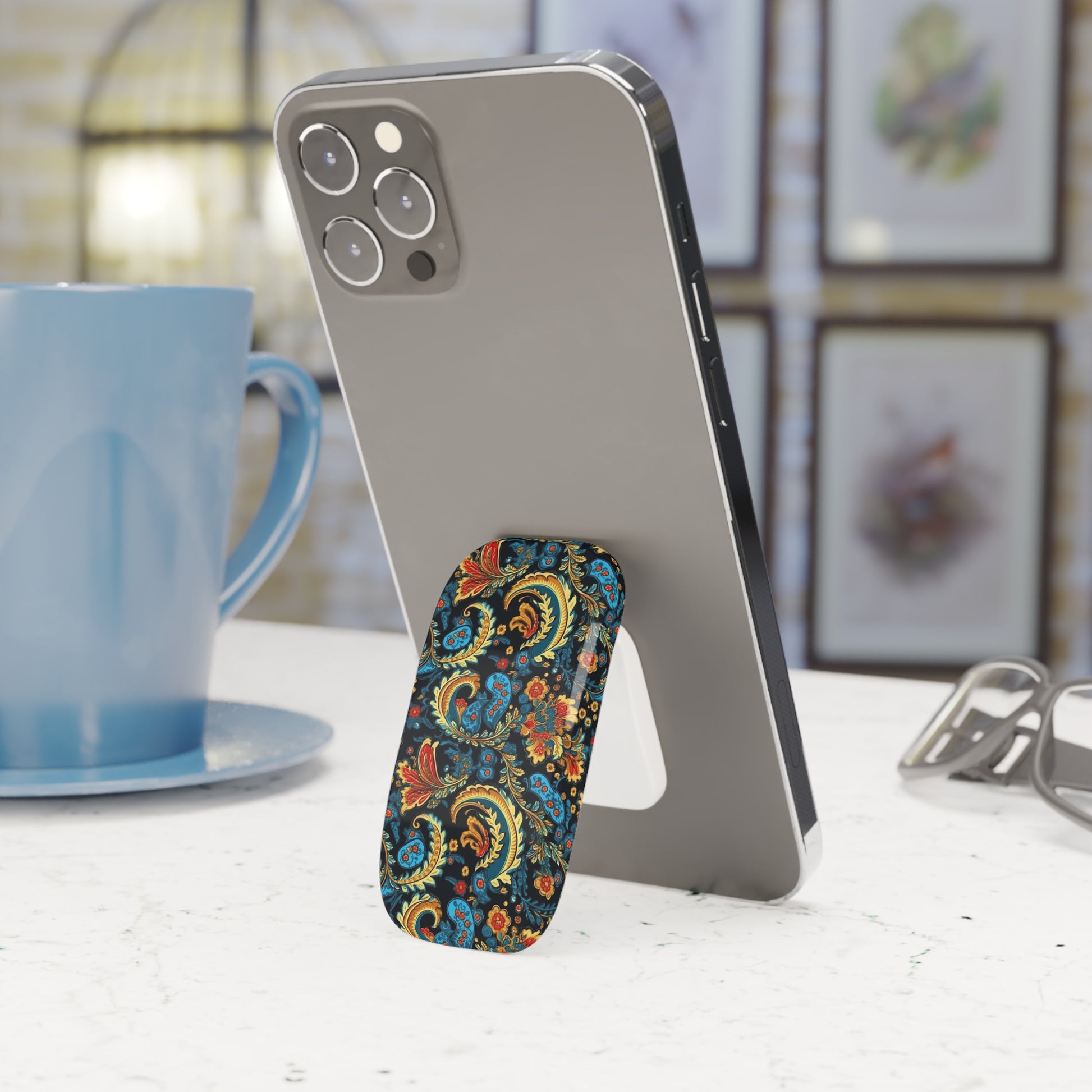 Phone stand with floral design next to a smartphone on a table with a blurred background