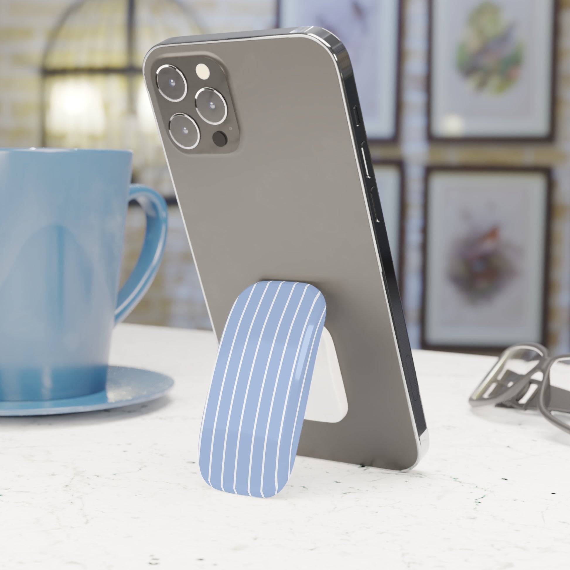 Phone stand with a phone on a table next to a blue mug
