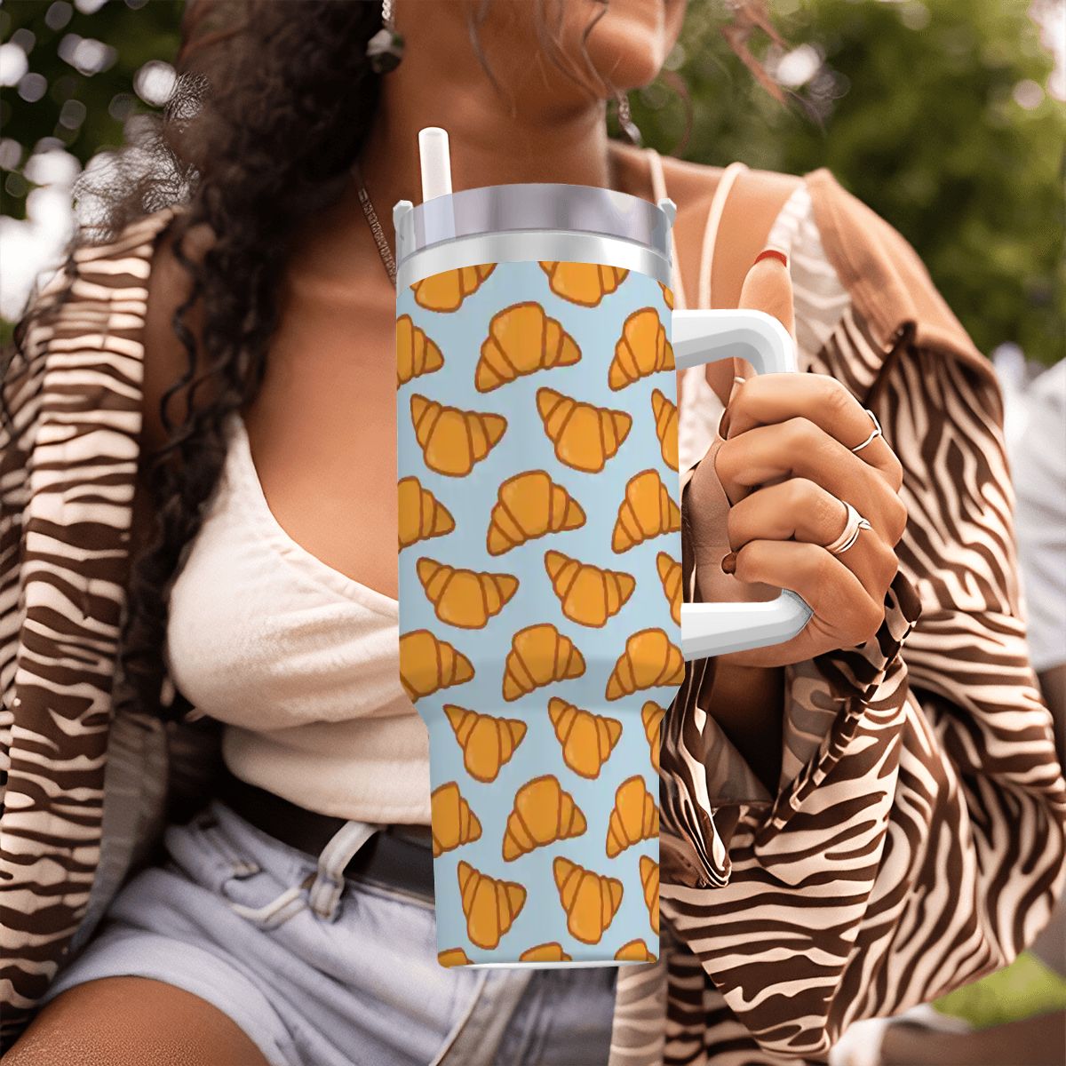Person holding a tumbler with croissant pattern outdoors