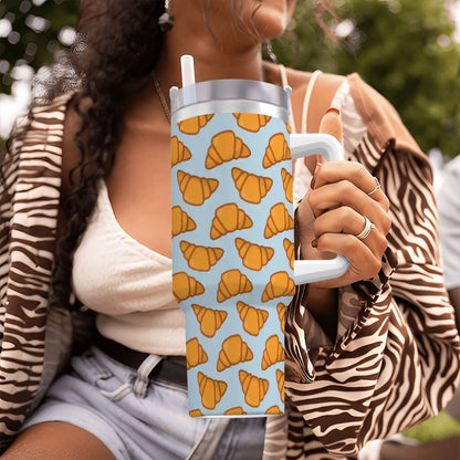 Person holding a tumbler with croissant pattern outdoors