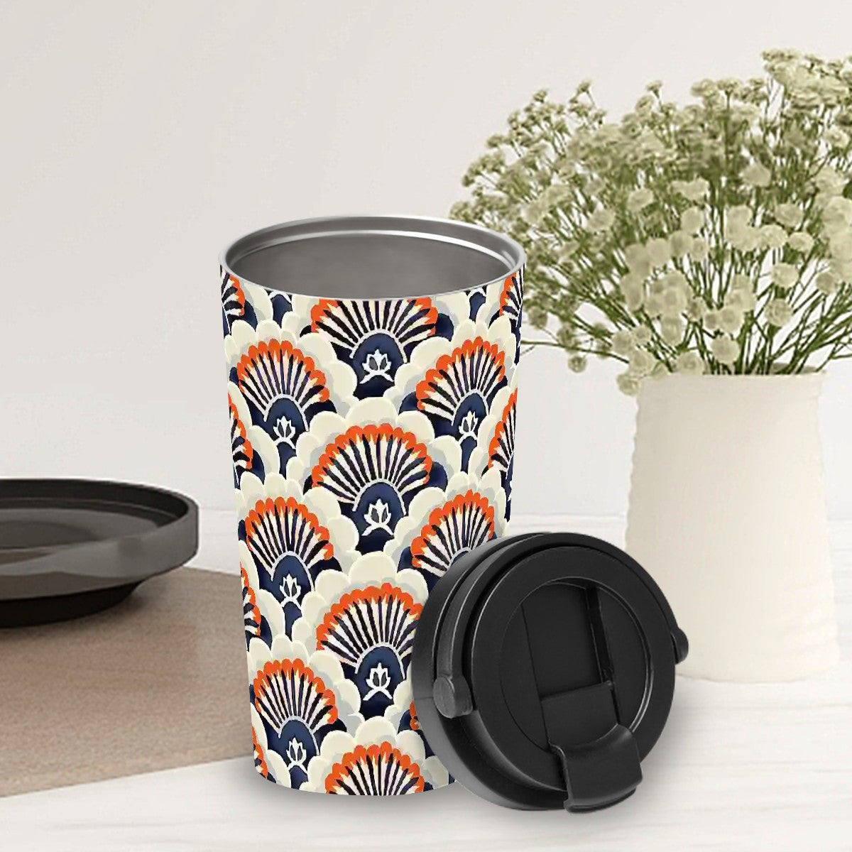 Travel mug with geometric pattern on a white surface with a vase of flowers in the background