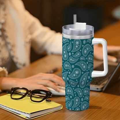 Teal patterned tumbler with a straw on a desk next to glasses and a notebook.