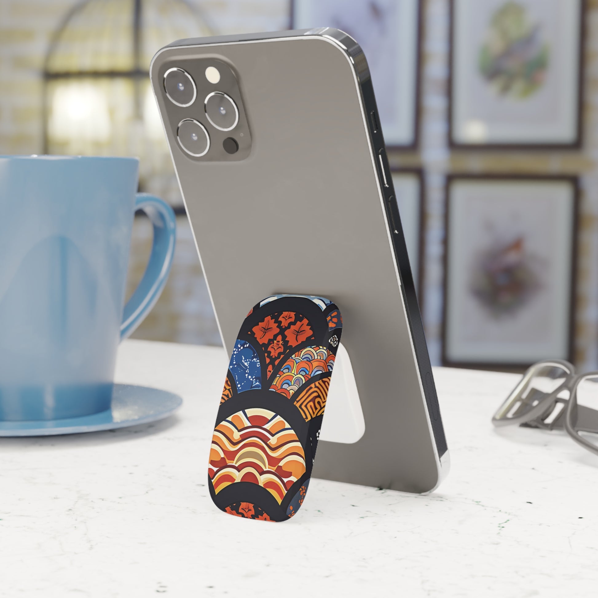 Phone stand with colorful design holding a phone next to a blue mug on a table. | Casenari