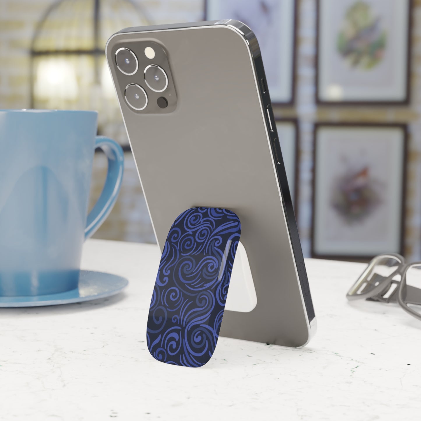 Phone with a blue patterned stand on a white surface next to a blue mug.