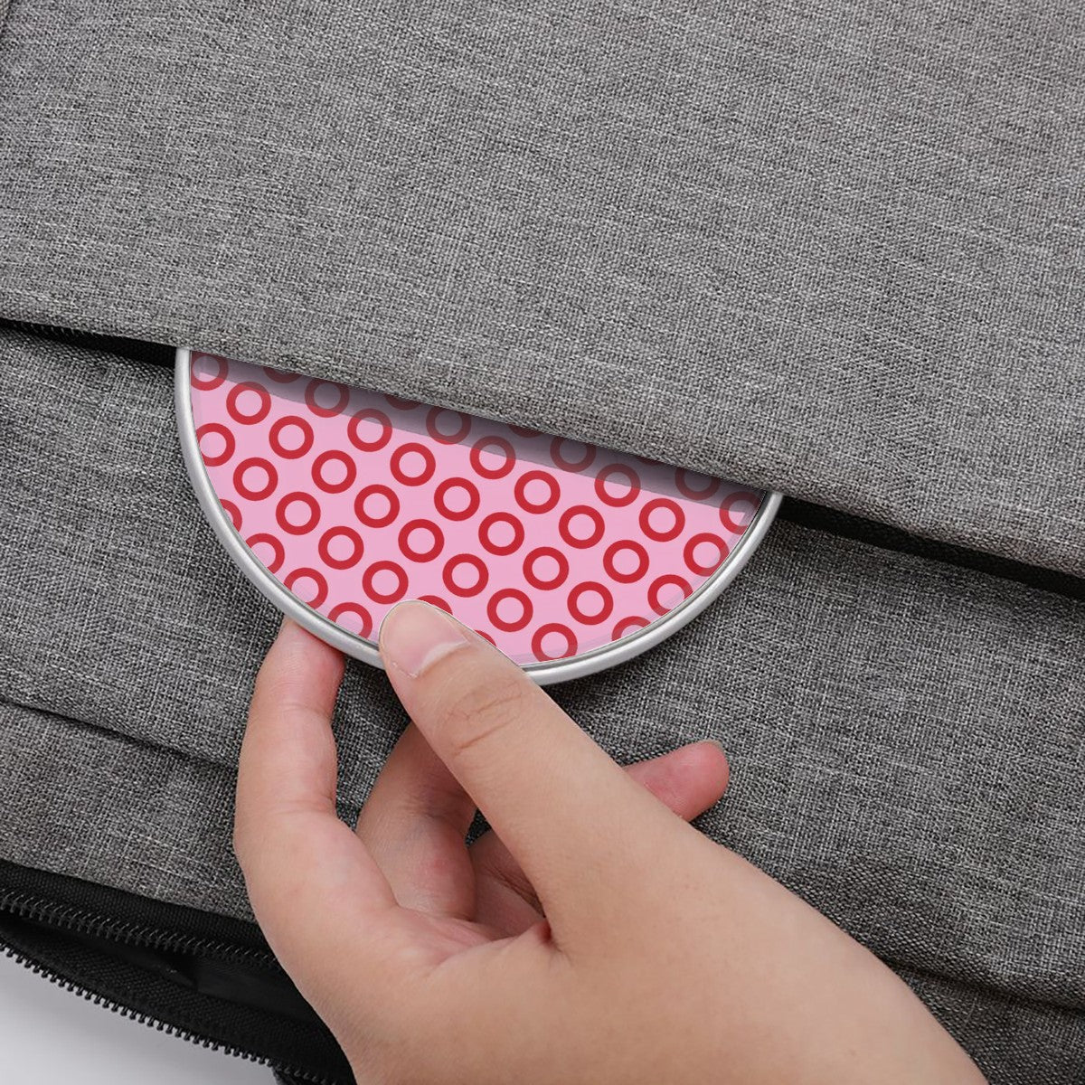 Hand opening a gray bag with a pink circular patterned compartment.