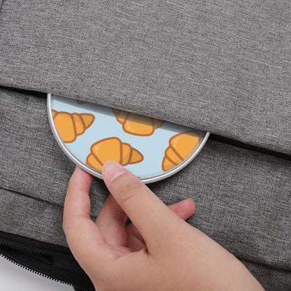 Hand opening a gray bag with a small round container featuring croissant designs. | Casenari