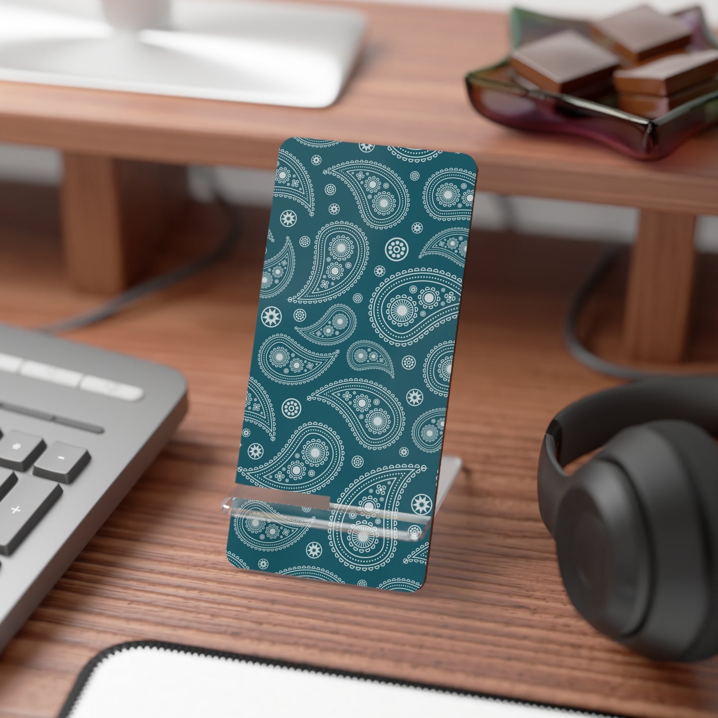 Teal patterned phone stand on a desk with a keyboard, mouse, and headphones.