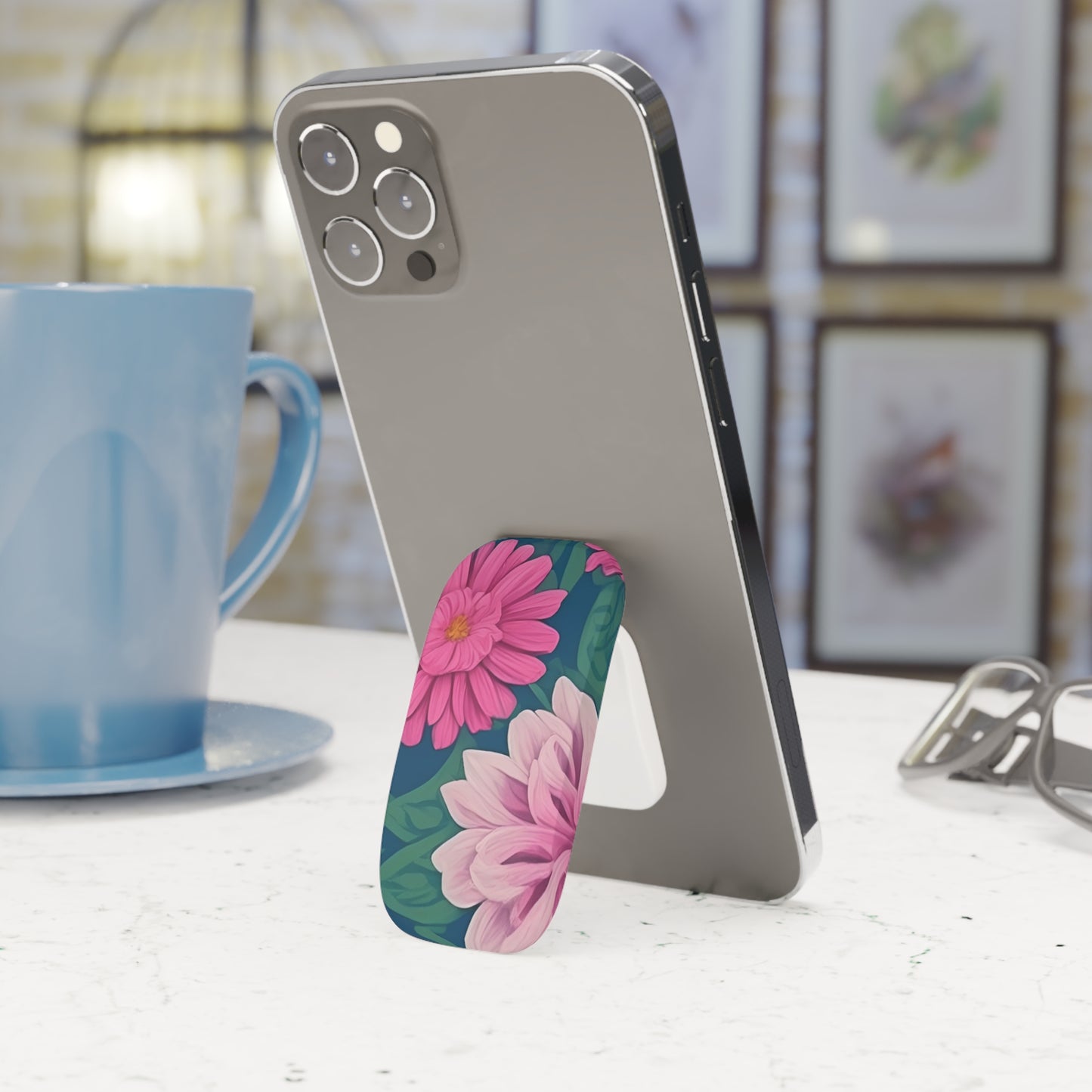 Smartphone with a floral phone stand on a table next to a blue mug.