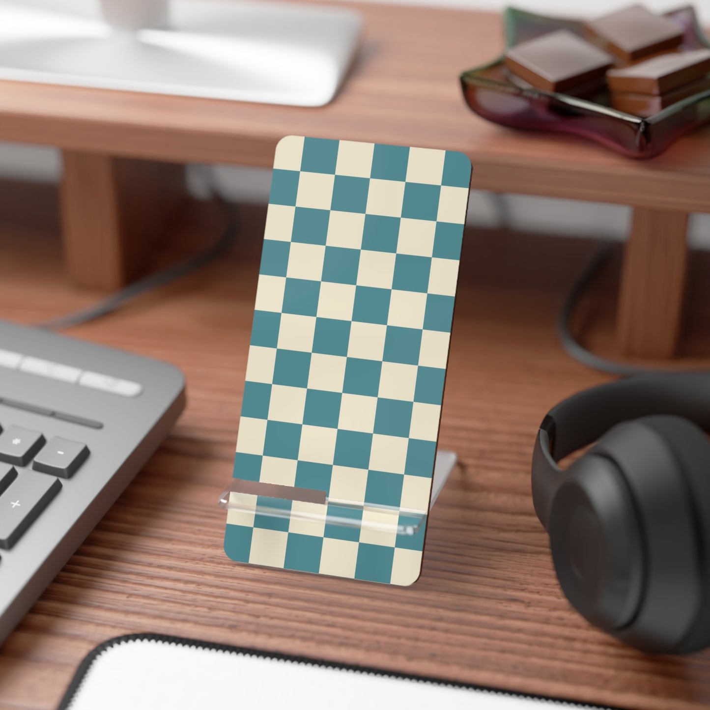 Checkered phone stand on a desk with keyboard, mouse, and headphones.