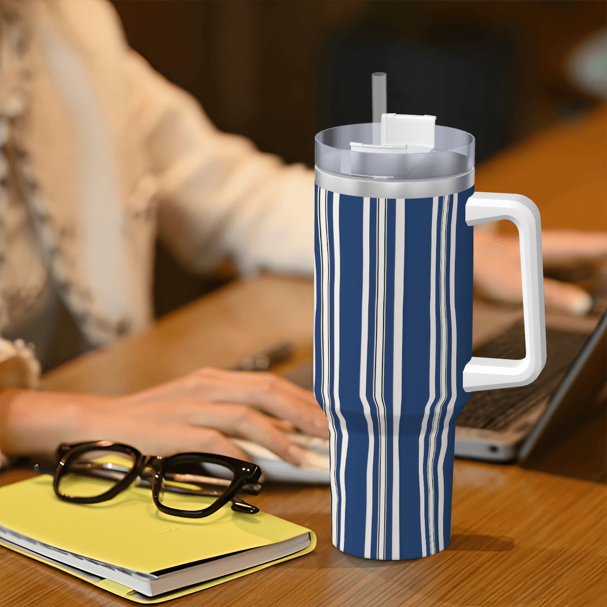 Blue and white striped mug with handle on a desk next to glasses and a notebook.