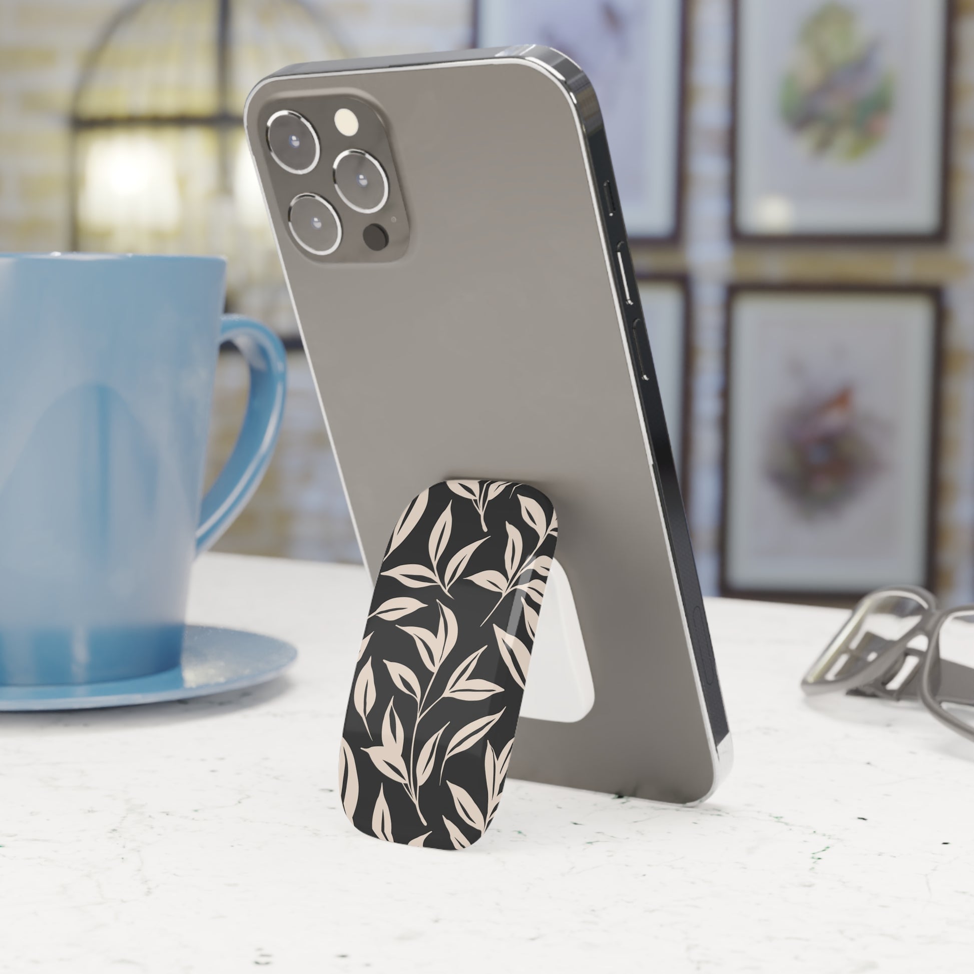 Phone with a floral stand on a table next to a blue mug