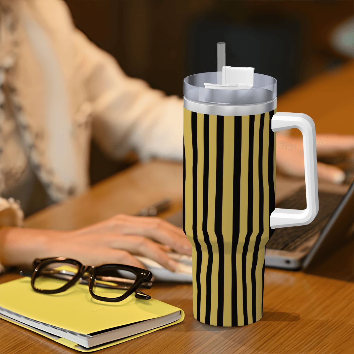 Black and yellow striped mug with handle on a desk next to glasses and a notebook.