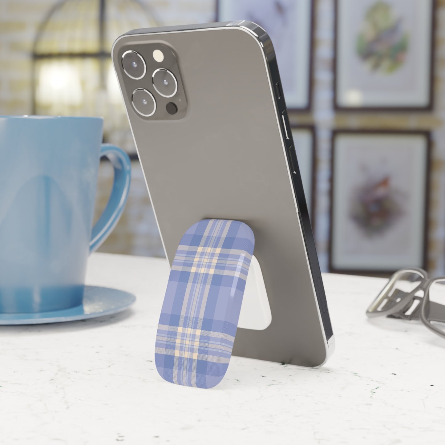 Phone with a blue plaid phone stand on a table next to a blue mug.